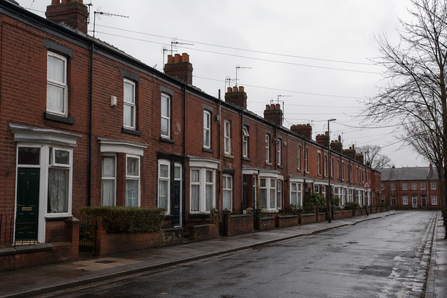 A street of red-brick Victorian terraced houses with TV aerials and overhead telephone drop wires on an overcast day