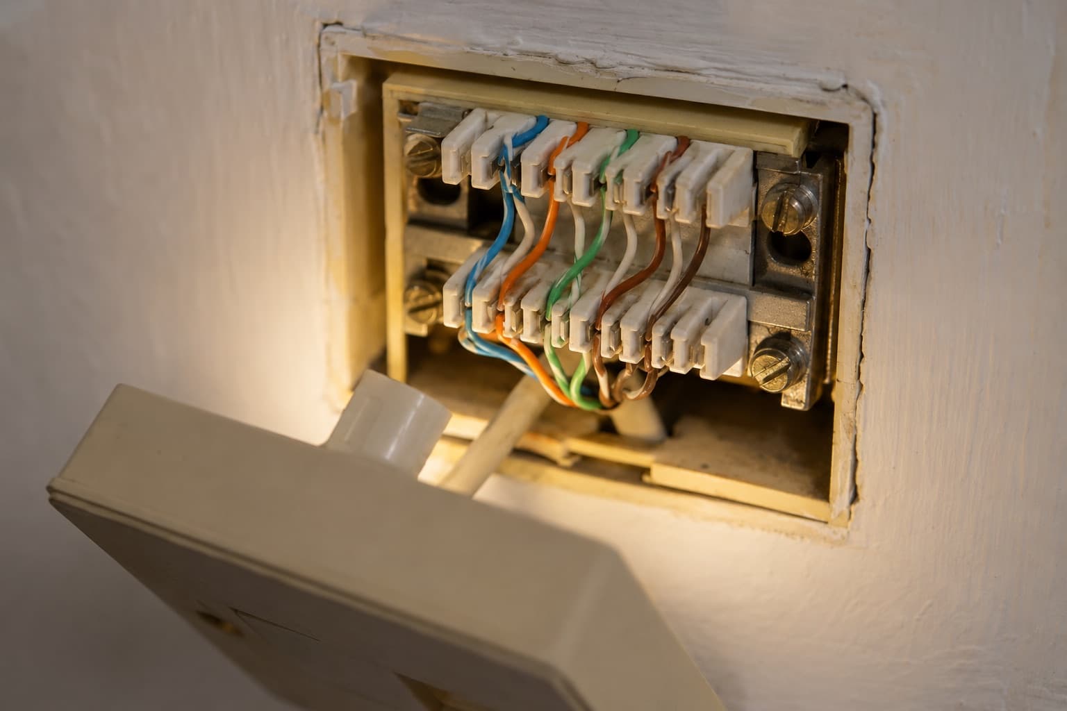 A BT master socket with the faceplate hanging forward, showing the punch-down terminals and the blue, orange, green and brown twisted pairs behind it